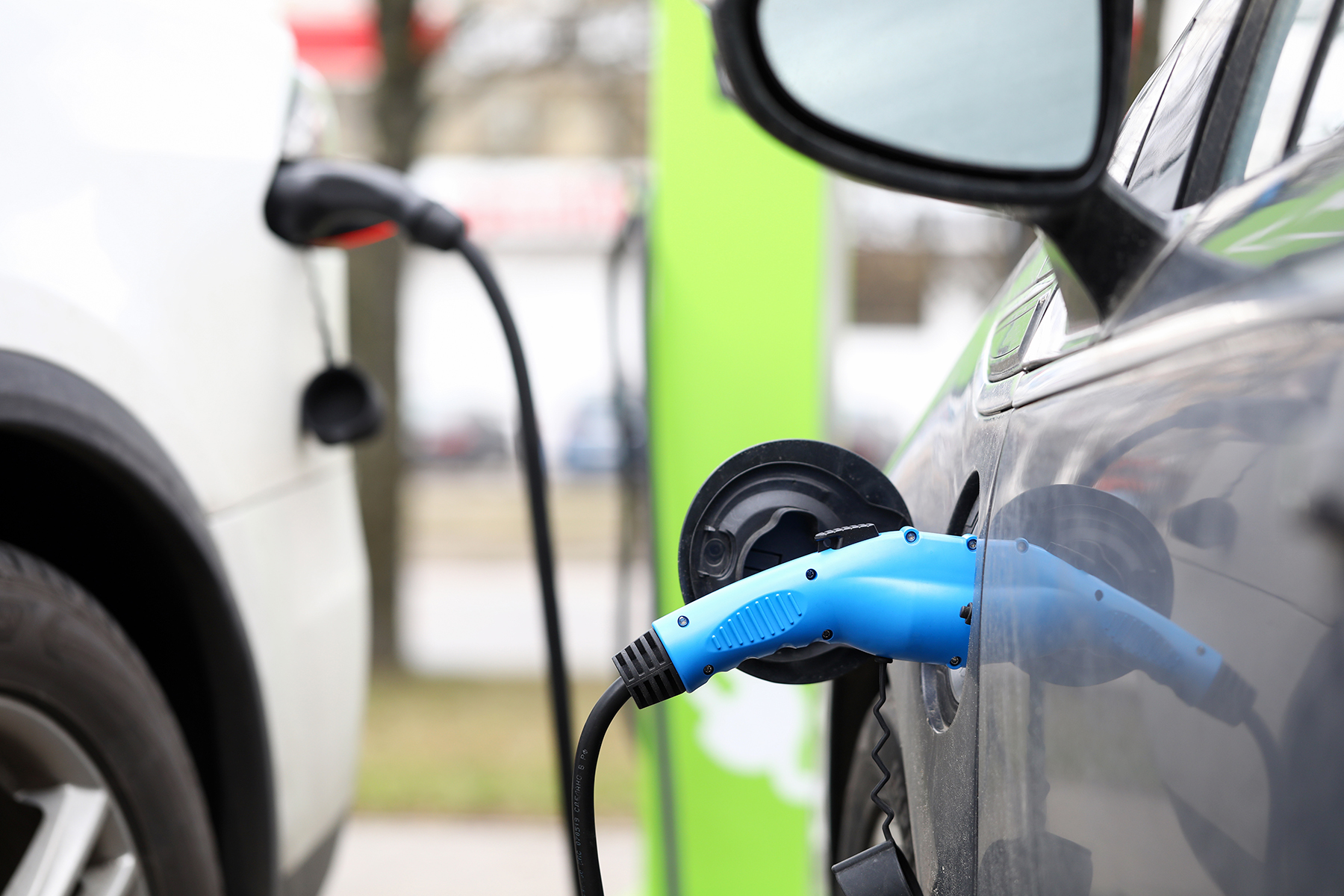 Zwei Elektroautos werden gleichzeitig an einer Ladestation geladen – Nahaufnahme eines blauen Ladekabels, das mit dem Ladeanschluss eines Fahrzeugs verbunden ist.